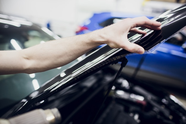 Las manos de los trabajadores instalan la cubierta protectora de la película protectora de la pintura del automóvil