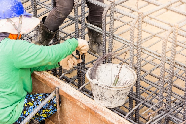 Manos de los trabajadores que usan alambre de acero y pinzas para asegurar las barras de refuerzo antes de que el concreto se vierta