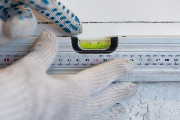 Las manos de los trabajadores verifican la uniformidad de la pared con una herramienta especial para medir el nivel La etapa de enfrentar la pared de la cocina con baldosas de cerámica blanca Reparación de restauración o trabajos de construcción