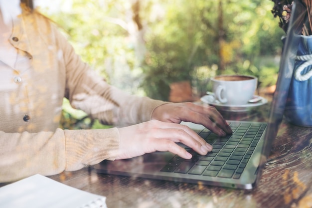 manos trabajando y escribiendo en el teclado del ordenador portátil en la mesa de madera en el café