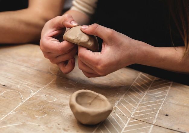 Foto manos trabajando y terminando escultura con arcilla en mesa de madera en taller