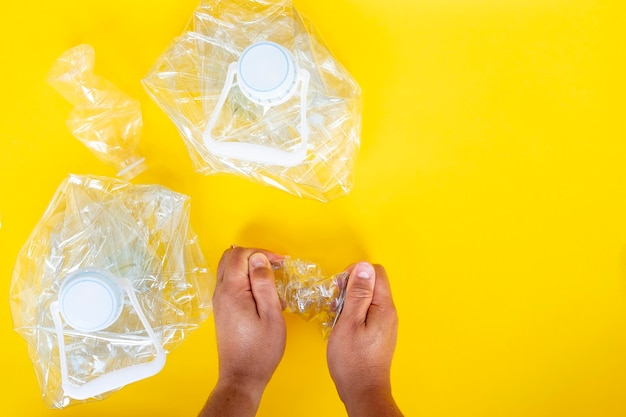 Manos triturando botellas de plástico para reciclar varias botellas de diferentes tamaños sobre fondo amarillo