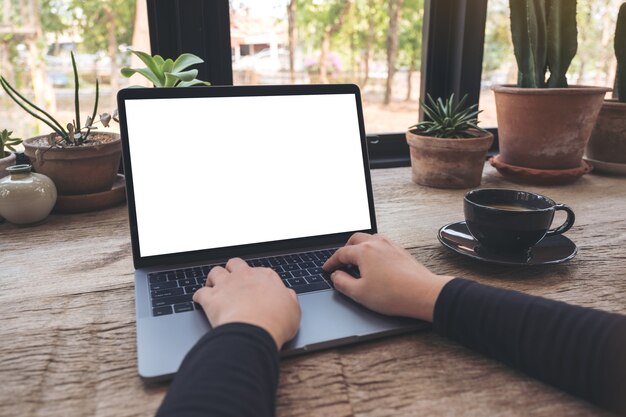 Foto manos usando y escribiendo en la computadora portátil con pantalla de escritorio blanco en blanco en la mesa de madera vintage