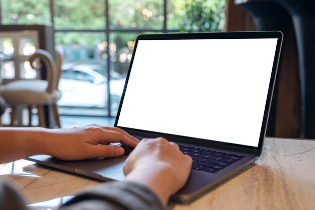 Foto manos usando y escribiendo en una computadora portátil con pantalla de escritorio en blanco mientras está sentado en la cafetería