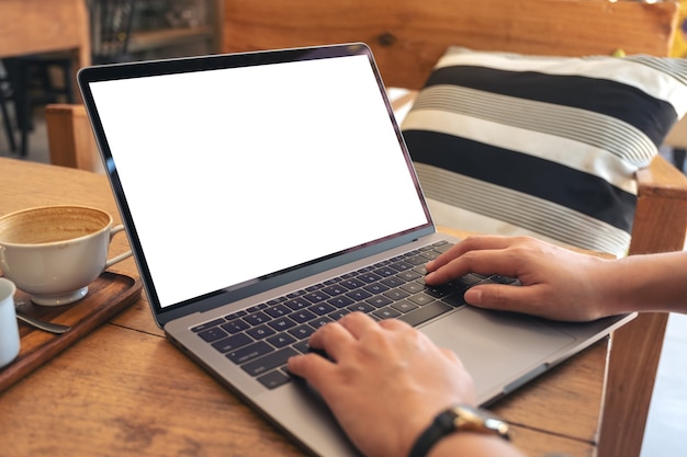 Manos usando y escribiendo en un portátil con pantalla de escritorio en blanco con una taza de café en la mesa de madera en el café