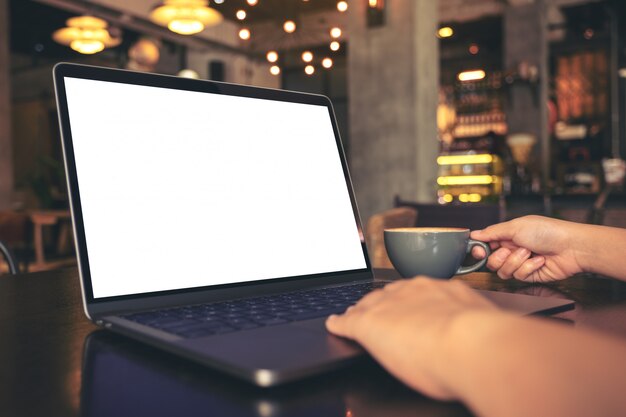 Manos usando laptop con pantalla de escritorio blanca en blanco mientras bebe café caliente