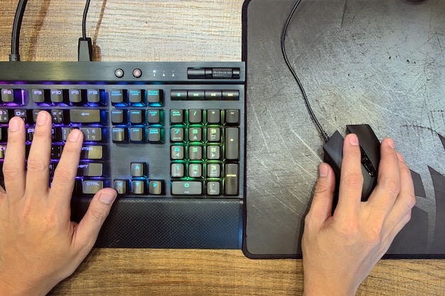 Manos usando un teclado con luces y mouse