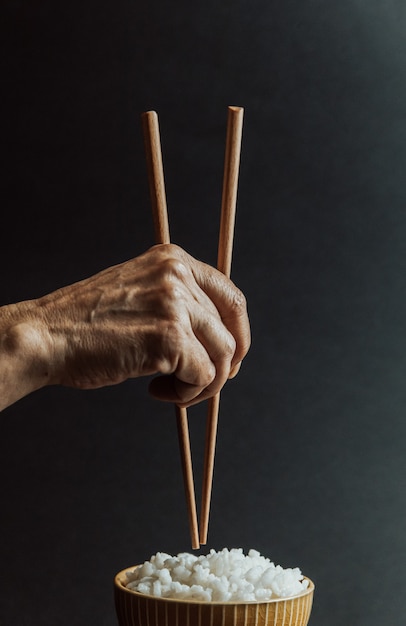 Foto manos viejas minimalistas agarrando palillos japoneses