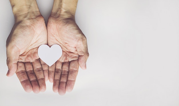 Manos del viejo hombre que llevan a cabo forma del corazón en el fondo blanco. Seguro de salud o concepto de amor.