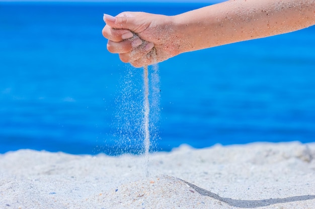A Las manos vierten arena del mar sobre la naturaleza en un viaje Vacaciones en el mar pasa el tiempo de arena