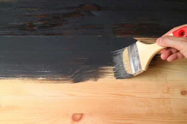 Mans mano pintando la superficie de la plancha de madera natural en color negro