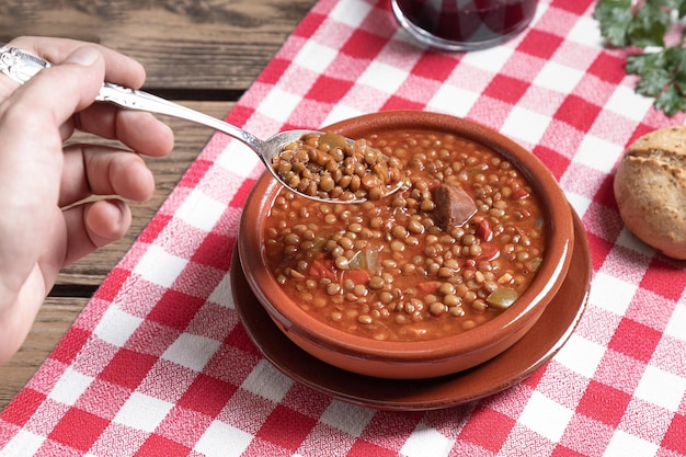 Mans mano recogiendo una cucharada de lentejas en la mesa de madera