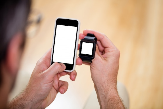 Mans mano sosteniendo un reloj inteligente y un teléfono móvil