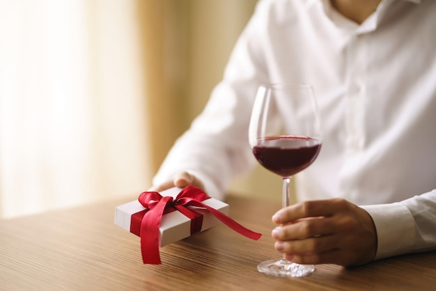 Mans manos con una copa de vino y un regalo Presente con una cinta roja