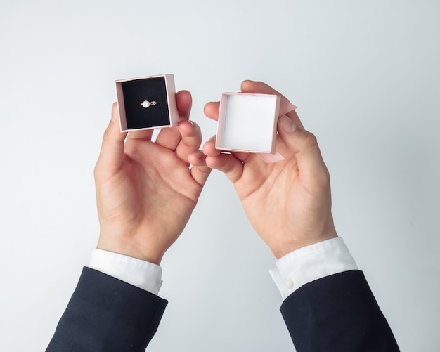 Mans manos sosteniendo una caja de regalo con un anillo de diamantes dorados sobre un blanco