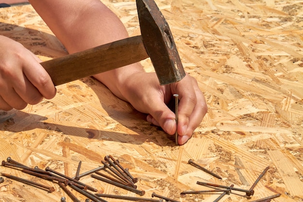 Mans martillando clavos en primer plano de la superficie de madera contrachapada. Manos masculinas jóvenes trabajan con martillo.