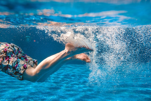 Mans piernas nadando bajo el agua en la piscina en verano