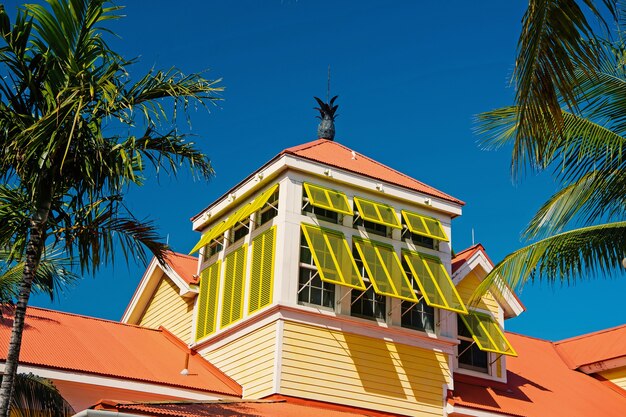 Mansarde mit offenen gelben Fensterläden und Ananas auf Terrakotta-Dach am sonnigen Tag am blauen Himmel