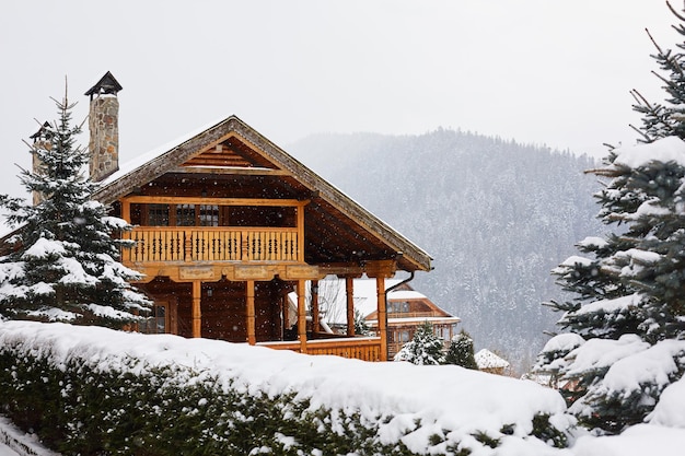 Mansión de madera navideña en las montañas en un día de invierno nevado Acogedor chalet en una estación de esquí cerca de un bosque de pinos Cabaña de madera redonda con balcón de madera Abetos cubiertos de nieve Chimeneas de piedra