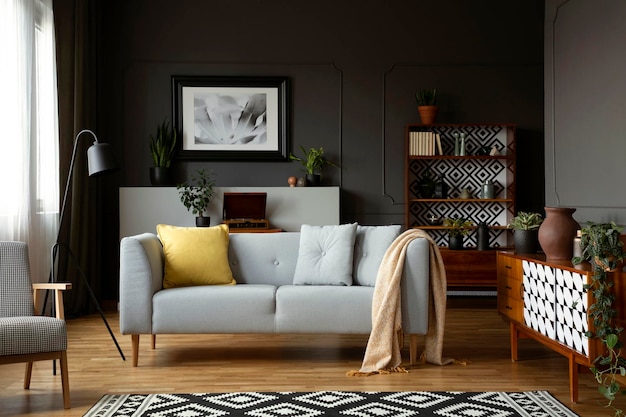 Manta y almohadas en un sofá gris en el interior de la sala de estar retro con sillón y póster Foto real