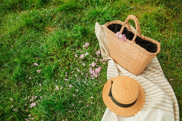 Manta de picnic con sombrero de paja y bolsa sobre hierba verde cubierta con flores rosas de sakura