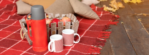 Manta vermelha e cesta com maçãs perto de garrafa térmica em um terraço
