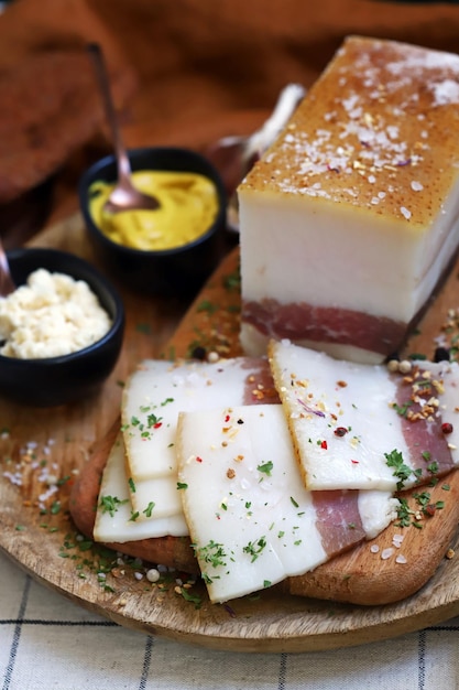 Manteca de cerdo fresca con capa de carne sobre una tabla de madera con especias, mostaza y rábano picante Delicioso bocadillo Tocino