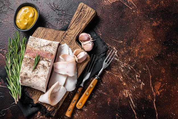 Manteca salada casera, rodajas con ajo y pimienta negra sobre tabla de madera. fondo oscuro Vista superior. Copie el espacio.