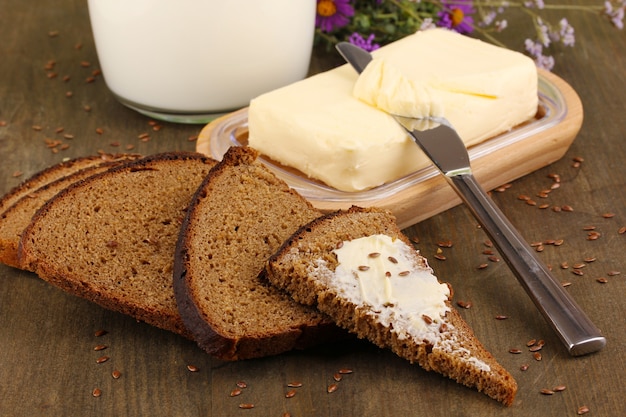 Manteiga em um suporte de madeira rodeada de pão e leite em close-up de mesa de madeira