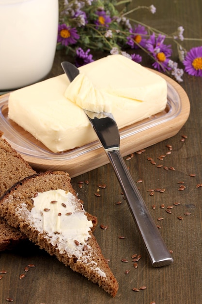Manteiga no suporte de madeira rodeado de pão e leite na mesa de madeira fechada