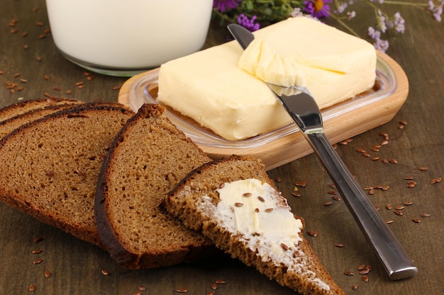Manteiga no suporte de madeira rodeado de pão e leite na mesa de madeira fechada