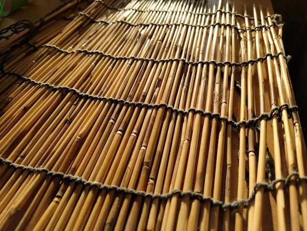 Un mantel de cama de paja o una alfombra pequeña colocados sobre una mesa y fotografiados desde un lado. La suave luz del sol del atardecer se refleja en los tallos. Algunos palos son hilos rotos y las cuerdas están trenzadas.