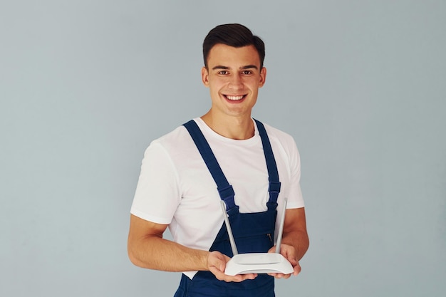 Mantém roteador wifi Trabalhador masculino em uniforme azul em pé dentro do estúdio contra fundo branco