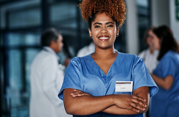 Foto mantendo sua saúde nas mãos de especialistas retrato de uma jovem médica confiante trabalhando em um hospital com seus colegas em segundo plano