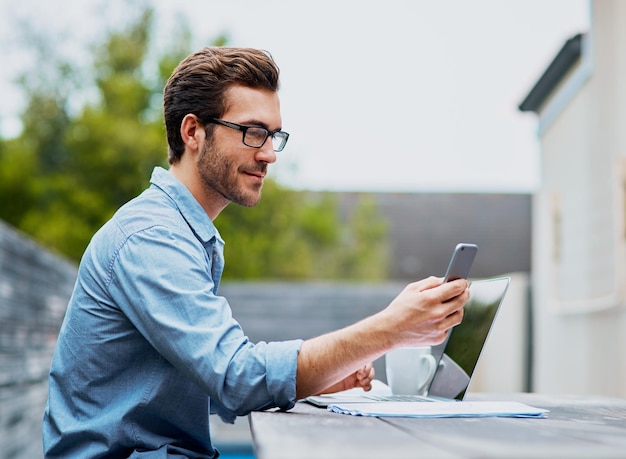 Mantendo todas as suas conexões ao redor Foto de um jovem bonito usando um laptop e celular ao ar livre