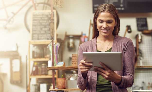 Foto mantendo um registro de seus objetivos de negócios em seu tablet foto de uma jovem empreendedora usando um tablet digital em sua loja