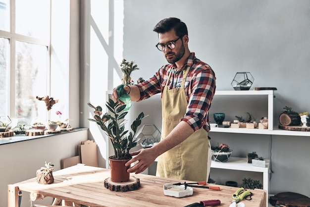 Mantener las plantas hidratadas. Apuesto joven en delantal regar la planta en maceta