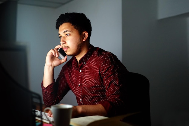 Mantenerse en contacto 247 Captura de un joven diseñador hablando por teléfono y trabajando en su computadora a altas horas de la noche