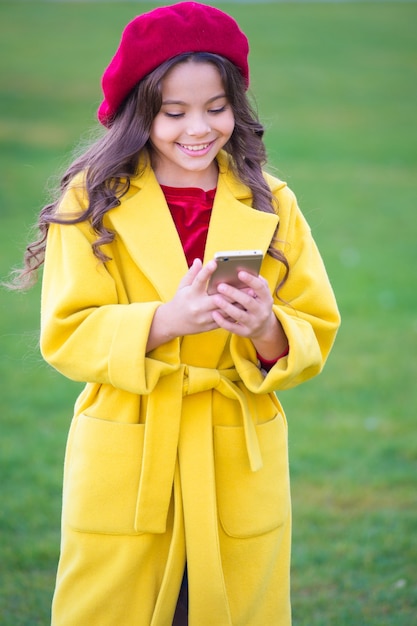 Mantenerse en contacto. Niña feliz lee sms en el teléfono móvil. Niña usa internet móvil el día de otoño. Infancia feliz y vida moderna. Disfrutando del otoño.