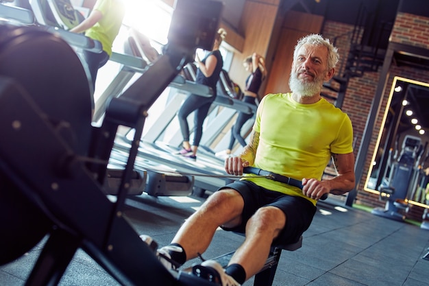 Foto mantenerse en forma y saludable hombre atlético maduro fuerte en ropa deportiva haciendo ejercicio en la máquina de remo en