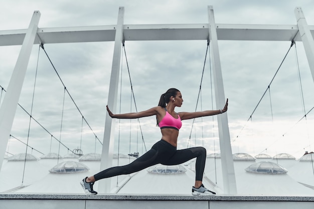 Mantenerse en forma y saludable. Mujer joven moderna en ropa deportiva que se extiende mientras se calienta al aire libre