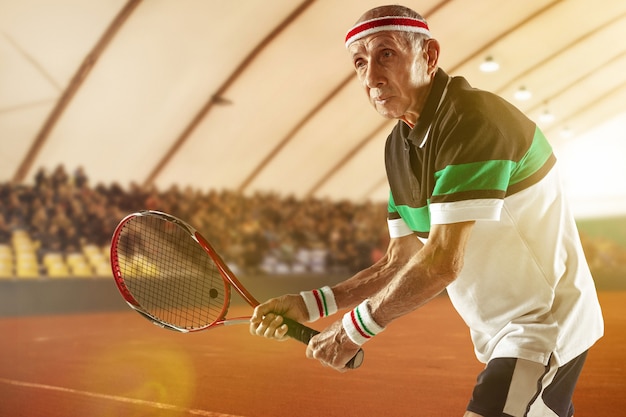 Mantenerse joven y saludable Senior hombre vestido con ropa deportiva jugando al tenis en el estadio