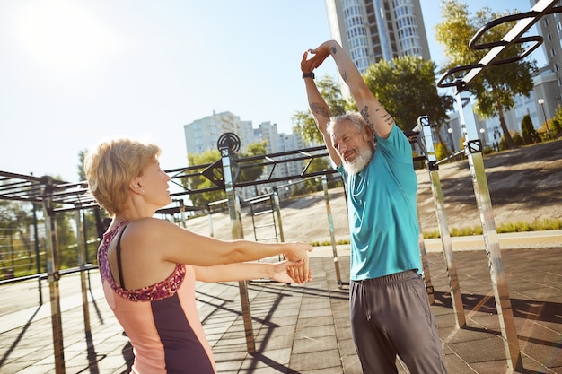 Foto mantenerse sano activo pareja de la familia madura en ropa deportiva calentando juntos en el gimnasio al aire libre en el