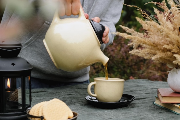 Mantenga caliente la fiesta del té de otoño Estado de ánimo de otoño Manos femeninas sirviendo té en una taza bebiendo té al aire libre