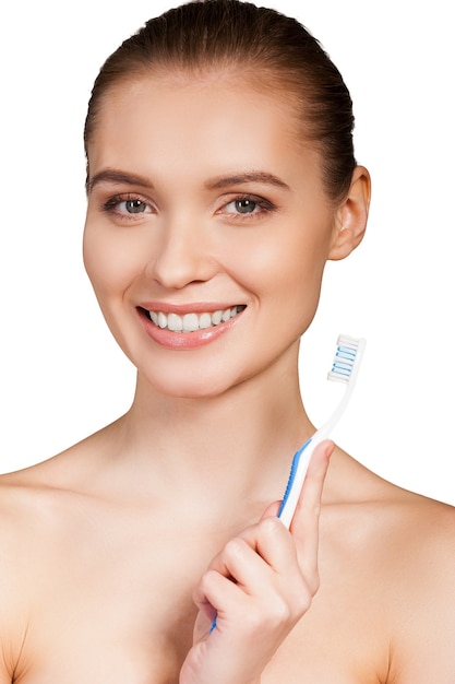 Manteniendo sus dientes limpios. Hermosa joven sosteniendo el cepillo de dientes y sonriendo a la cámara mientras está aislado sobre fondo blanco.