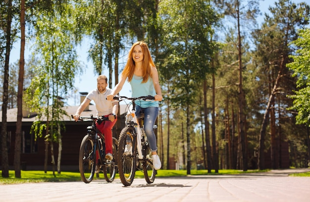 Manteniéndose en forma. Mujer bonita exuberante sonriendo y andar en bicicleta con su marido