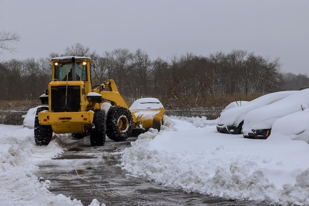 Mantenimiento de carreteras del tractor quitanieves quitando la nieve en el estacionamiento para el coche después de las nevadas