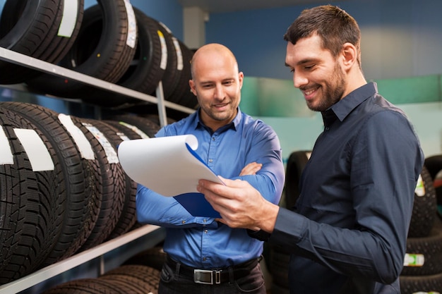 Foto mantenimiento de negocios y concepto de personas cliente masculino que elige discos de rueda y vendedor con clipboard en un servicio de reparación de automóviles o tienda de automóviles