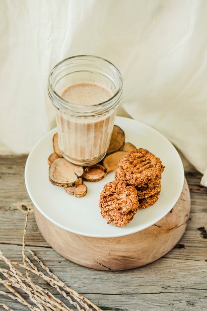 Foto mantequilla de cacahuete sin gluten, harina de avena y dátiles sin harina con un vaso de leche sobre madera