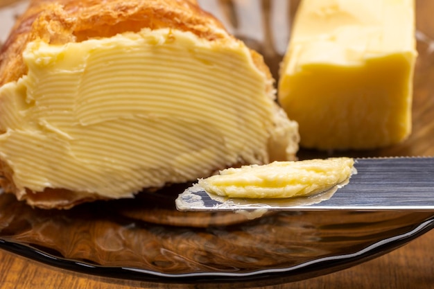 Foto mantequilla en cuchillo y croissant. pedazo de mantequilla en platillo. de cerca